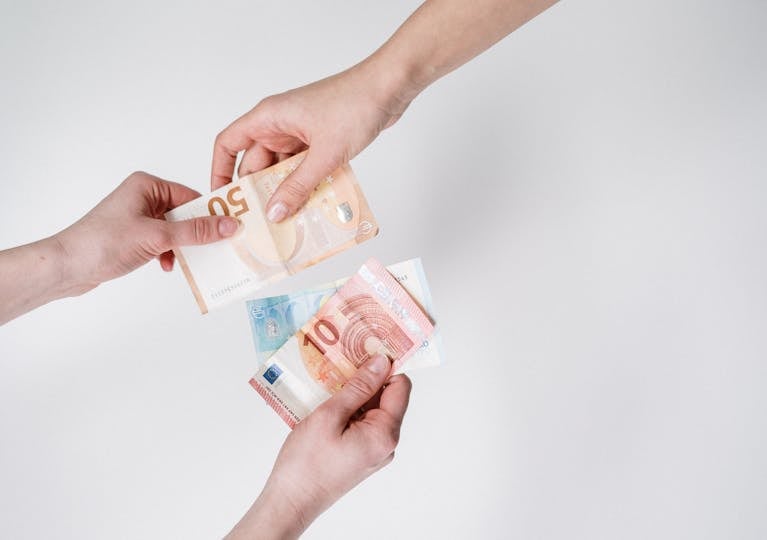 Zwei Hände tauschen Euro-Scheine, darunter ein 10-Euro-Schein und ein 50-Euro-Schein.