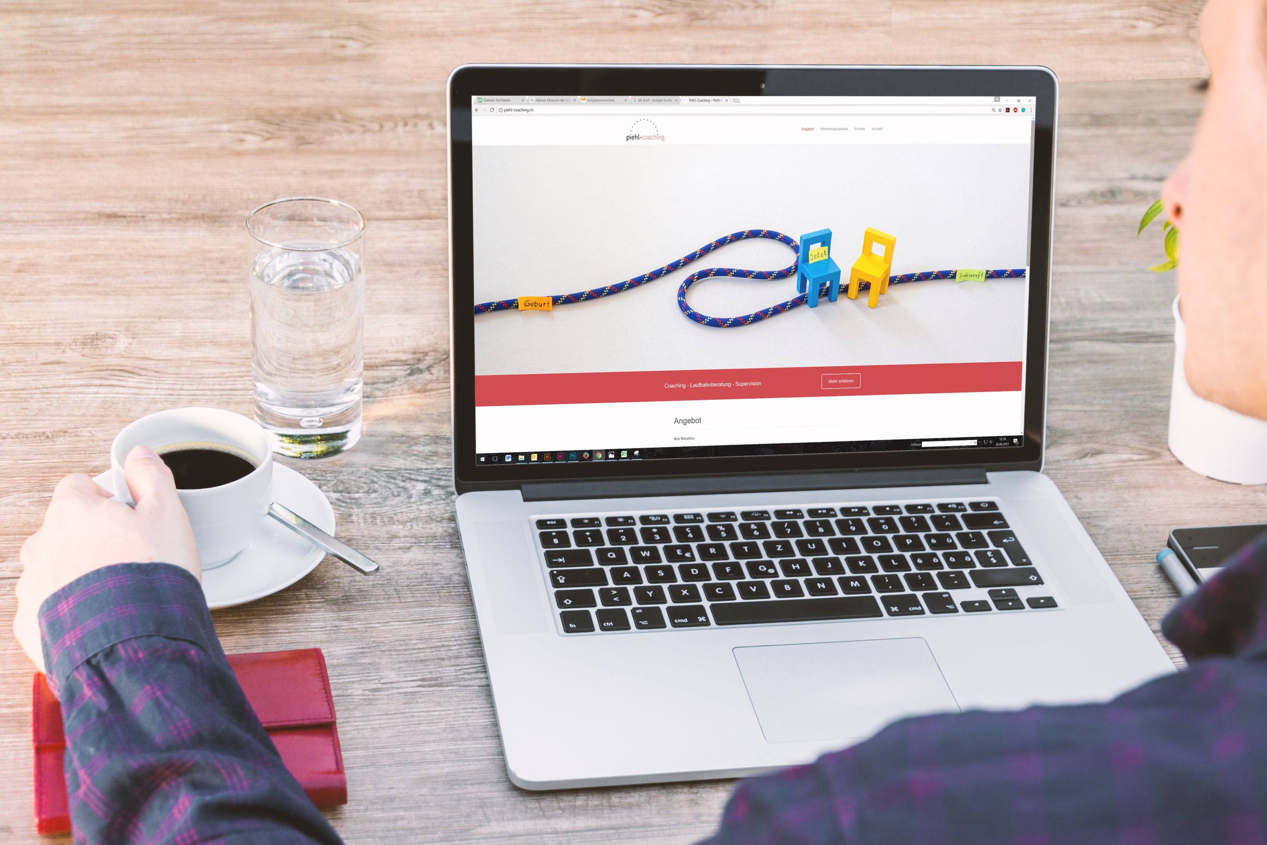 Laptop, Kaffeetasse und Wasserglas auf einem Schreibtisch